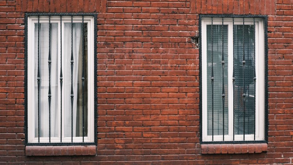 Two tall white-framed windows with black iron bars set in a red brick wall