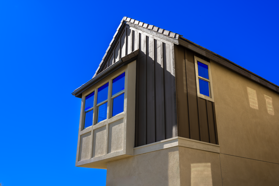 Corner of a two-story house with a bay of small windows and a single window against a deep blue sky