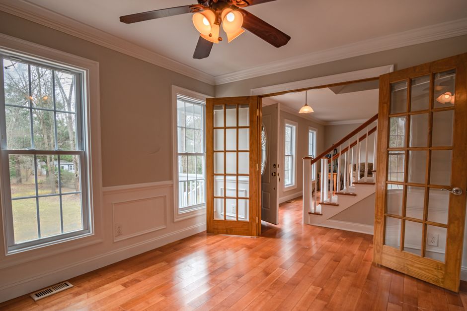 Living room with tall double hung windows, wooden French doors, hardwood floor and a ceiling fan