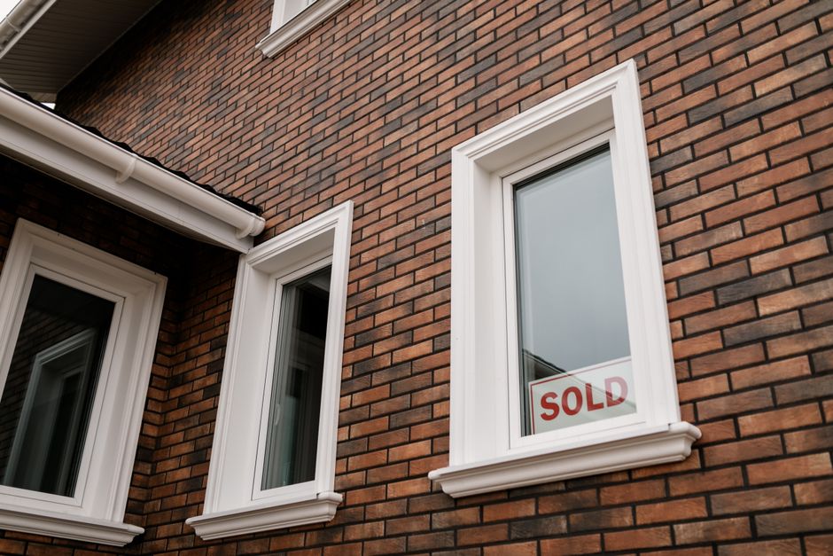 Three white-framed windows in a red-brown brick wall, one with a sold sign visible behind the glass
